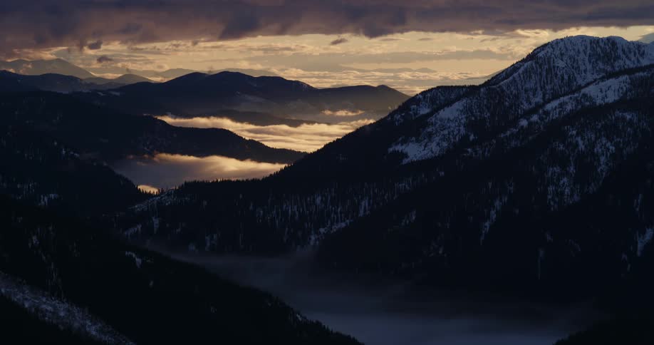 Sun setting behind mountain range with lakes and snow