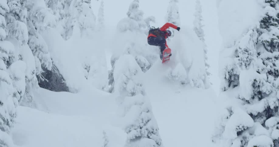 Snowboarder goes over ski jump in snowy forest
