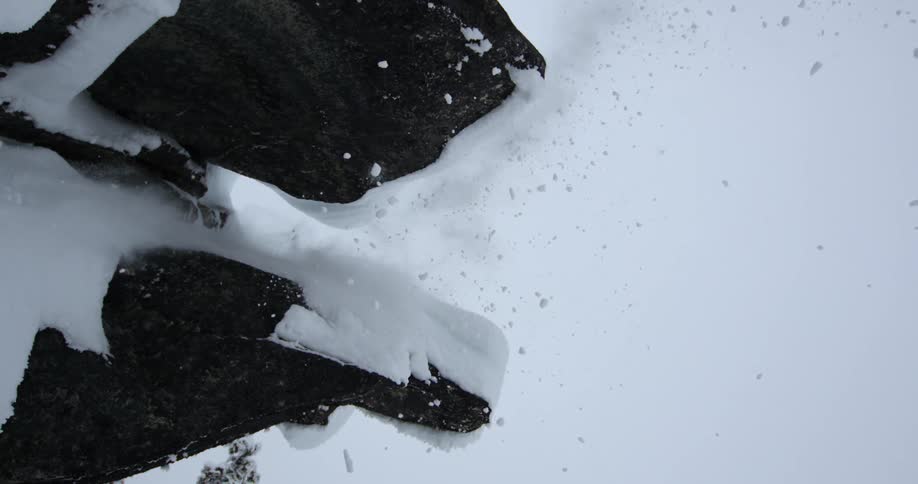 Skier jumps off snow covered ledge against clear blue sky setting off a fall of snow