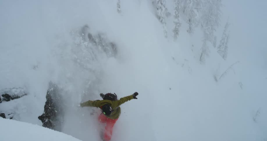 A snowboarder wearing a backpack goes over and down a steep fall