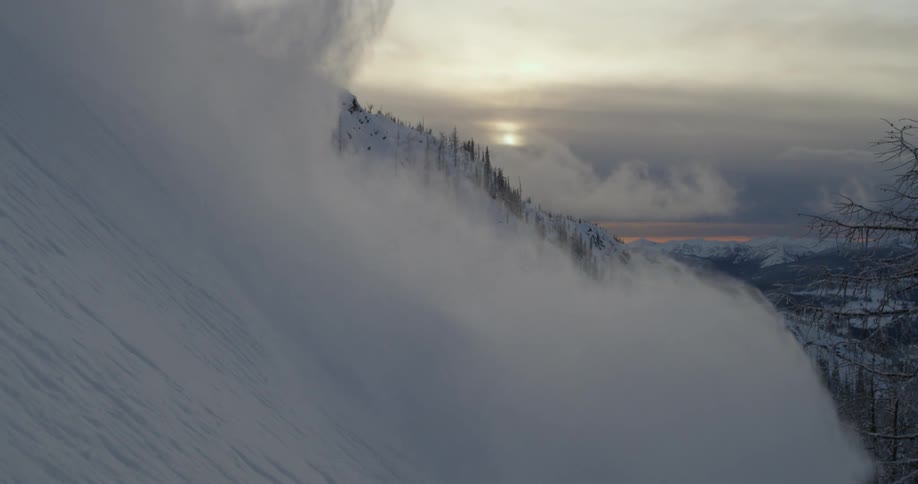 Skier slides down the snow covered mountain slope at sunset