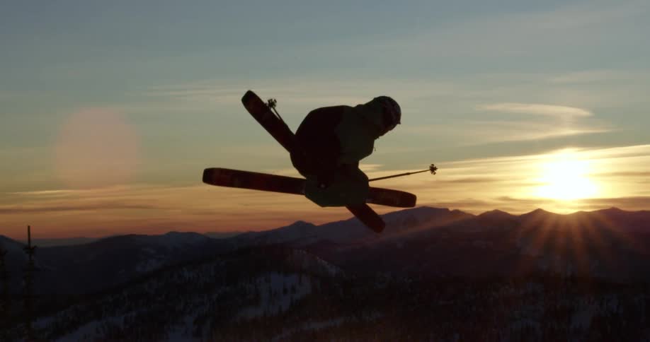 Person skis over ski jump in front of mountains at sunset