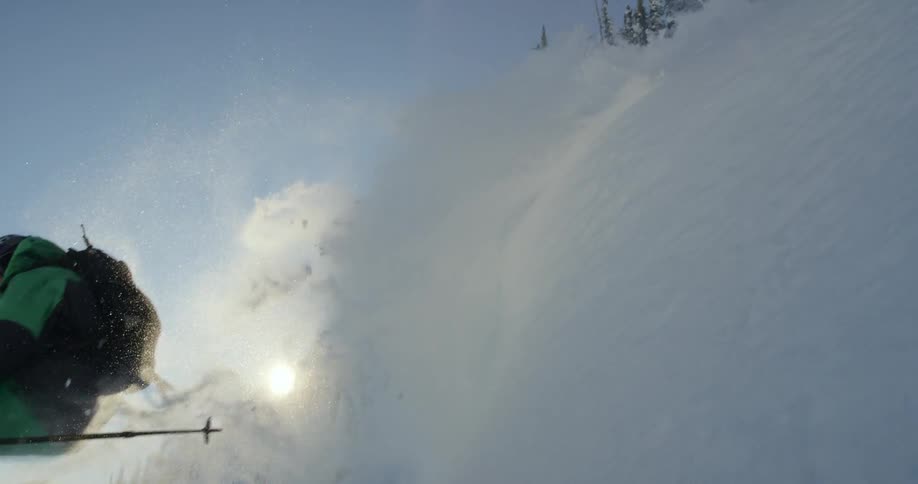 Sun peaks over mountain as skier jumps down slope past conifers