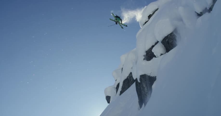 Skier jumps down slope spinning in midair