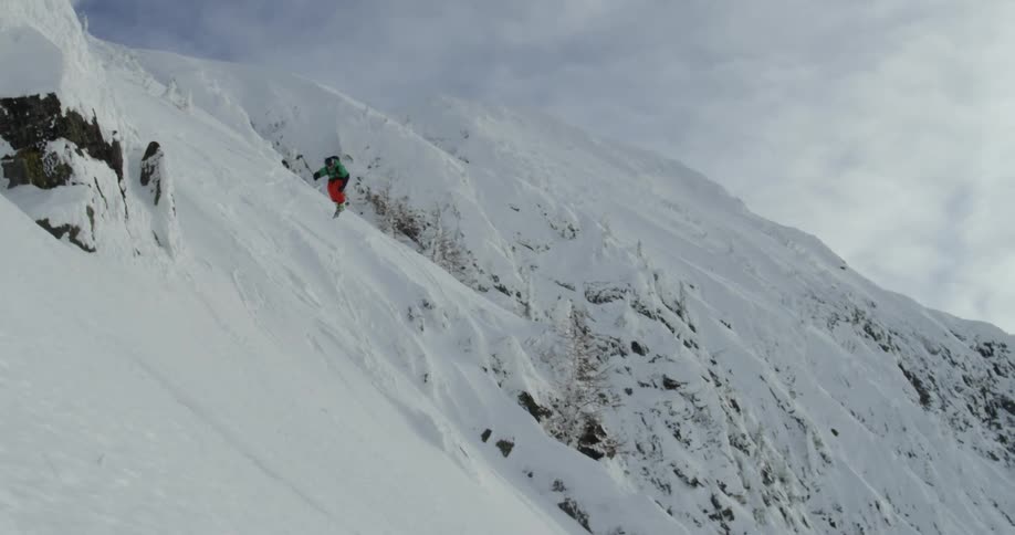 Skier jumps from high ridge onto slope below in rugged mountains