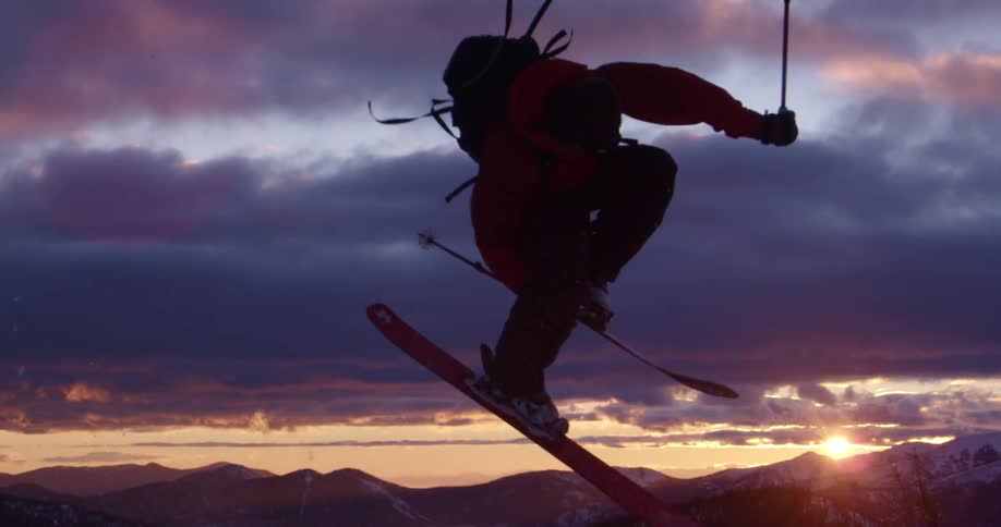 Person jumps on skis in front of mountains at sunset