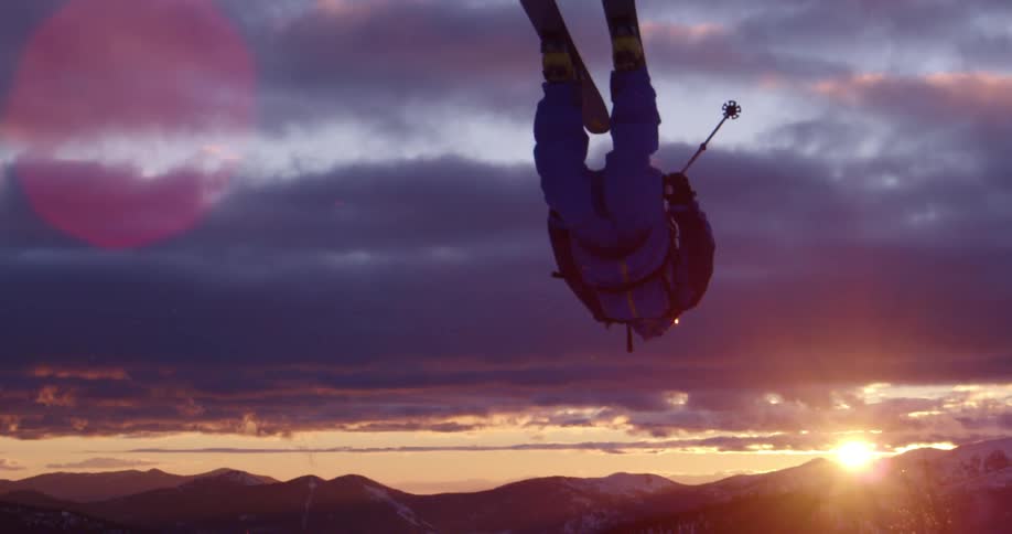 A skier does a backflip as they flip through the air before falling out of frame