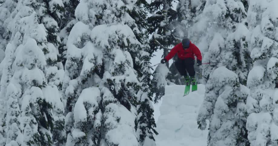 A skier going over a jump in a snowy mountain forest