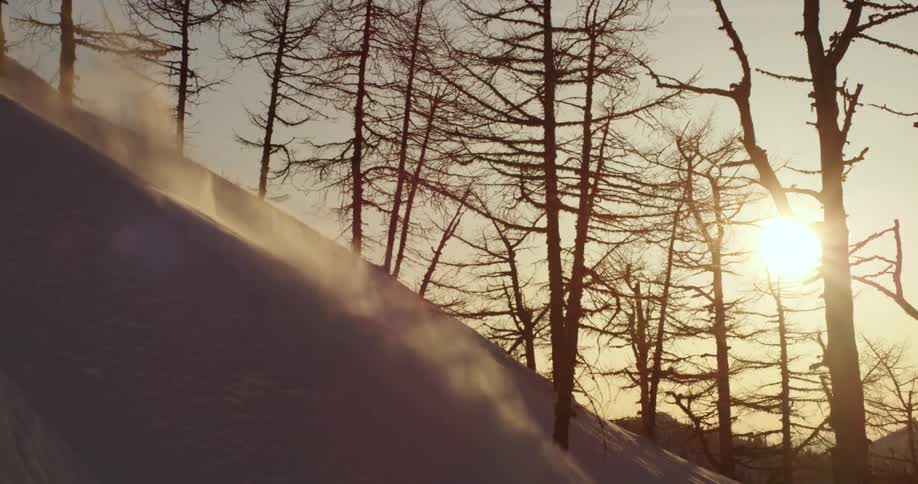 Man on a snowboard slides down the snow covered hill in the mountains at sunset