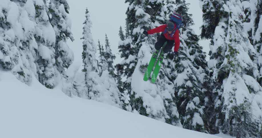 A skier does a jump flip over snow covered trees