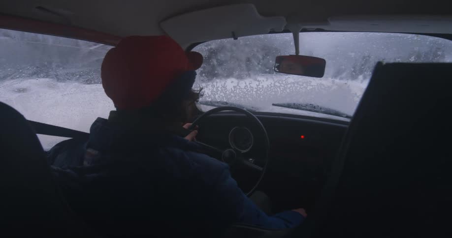 A man driving his car with an iced up windshield down a snow covered road