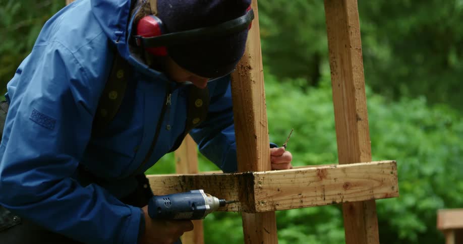 A man uses a drill on a screw in wood