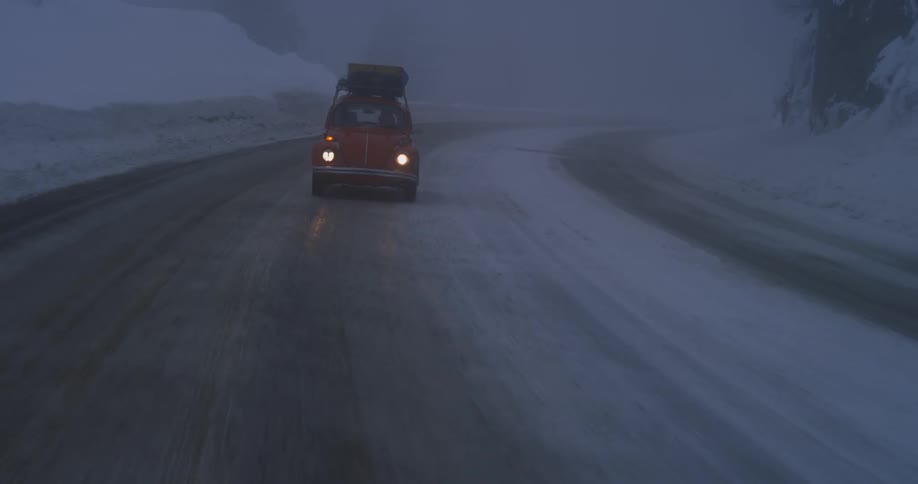 An old beetle is driving on an icy road at dusk