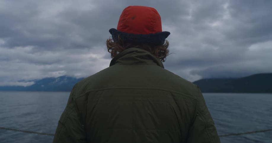 A person stands on a ship looking out at the mountains