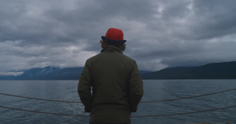 A man stands on a ferry and looks out at the water