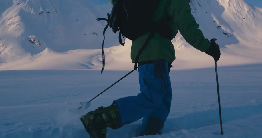 Man walking from a tent camp to the mountains on skies over the thick snow at sunset