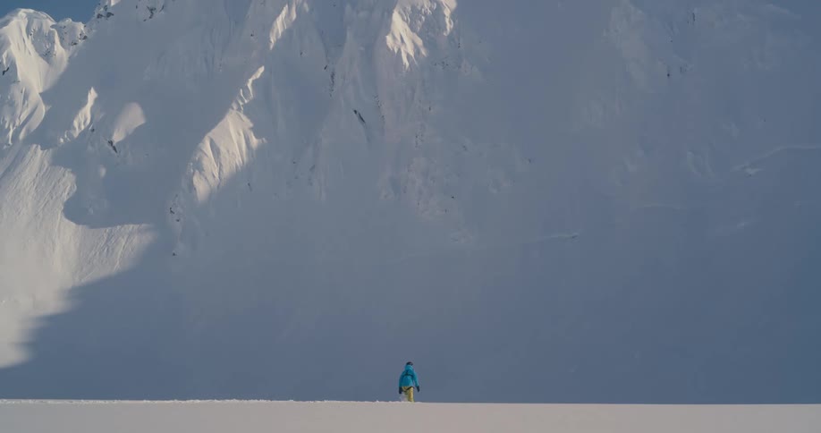 A person walks through deep snow towards a steep snow covered slope