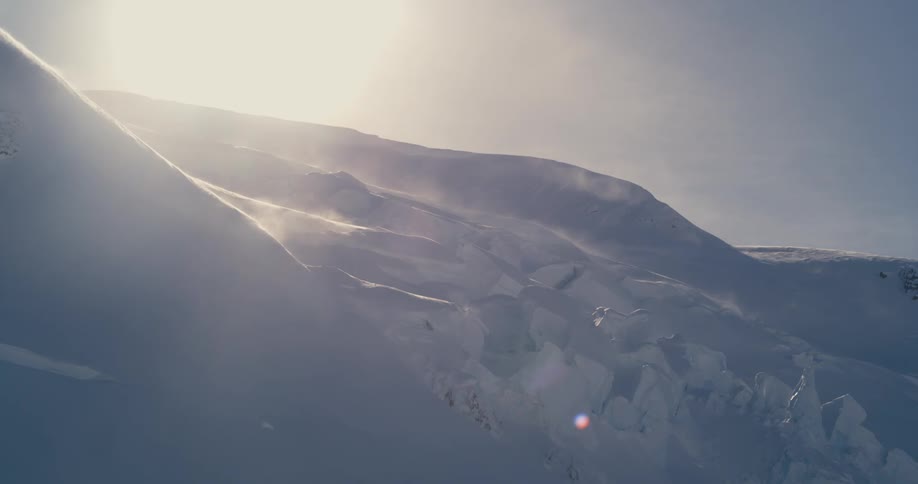 A mountain range covered in snow with the sky clouds and the sun in the background