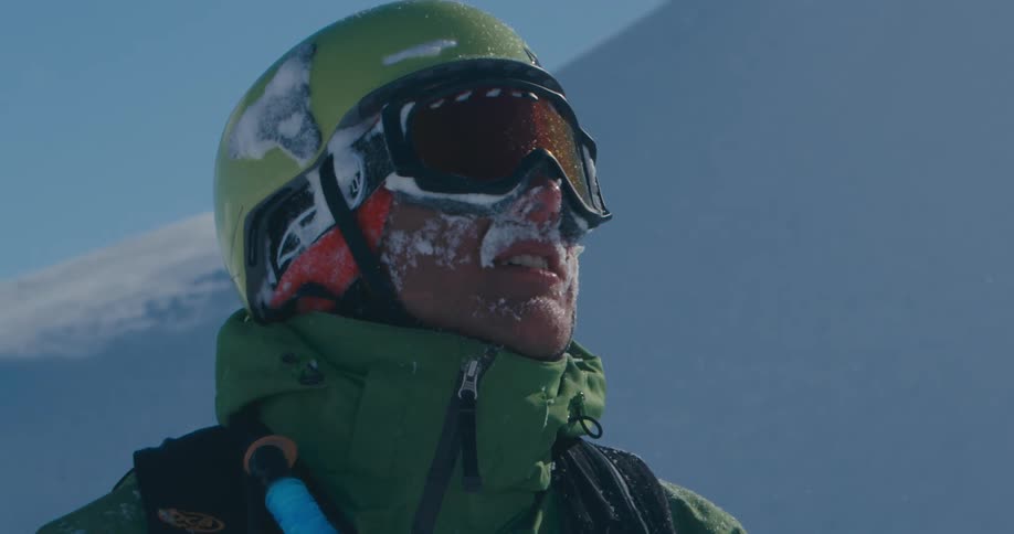 A man looks at a mountain and turns his head and reveals his face covered in snow