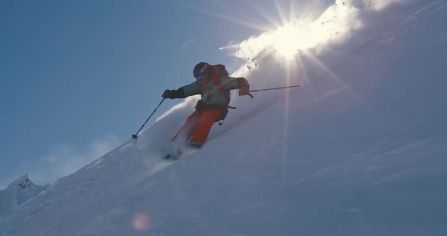 A person with a jacket and helmet skiing down a snow covered mountain with the sky in the background