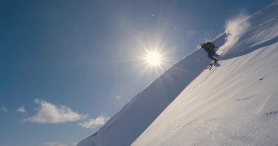 A skier descends a steep mountain slope on a sunny day