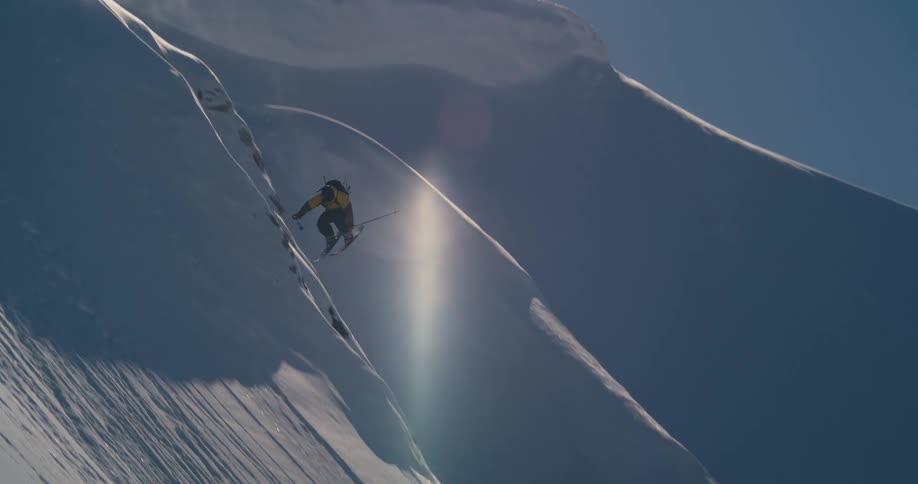 A person with a backpack and helmet skiing down a snowy slope with the sky in the background