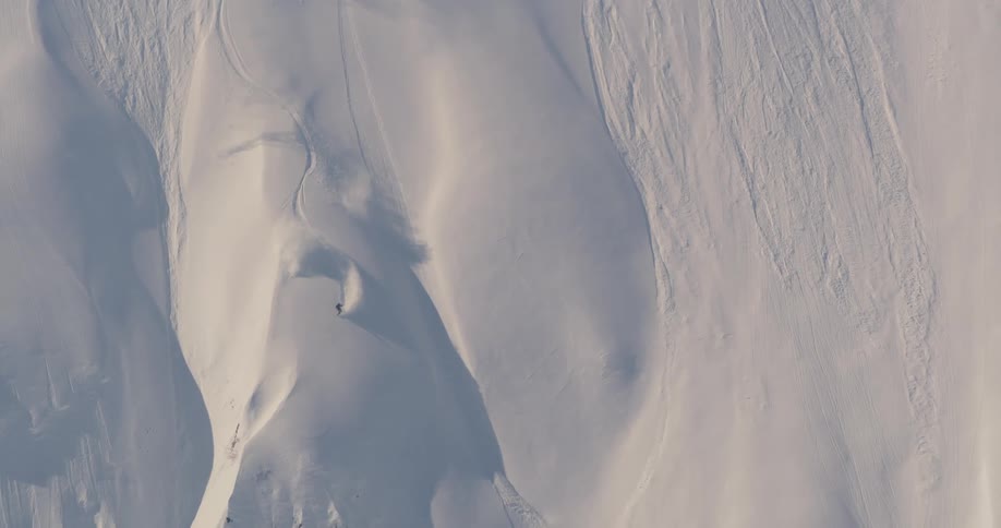 An aerial view of a skier speeding down a snowy mountainside