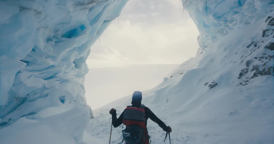 A man is hiking in a snowy and icy environment during the daytime