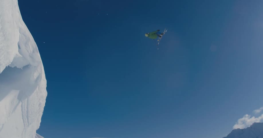 A person skiing down a snow covered mountain flips twice while in mid air