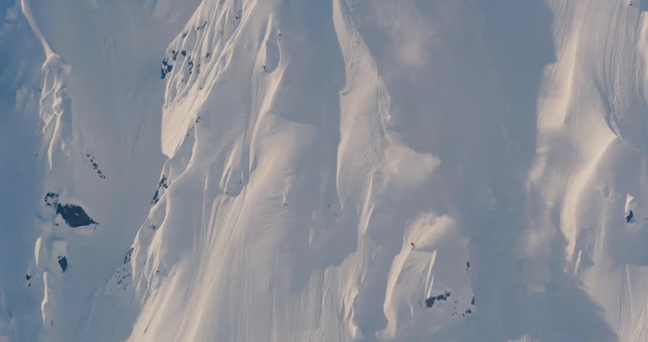 Skier skis down steep snow covered mountain slope causing mini avalanches
