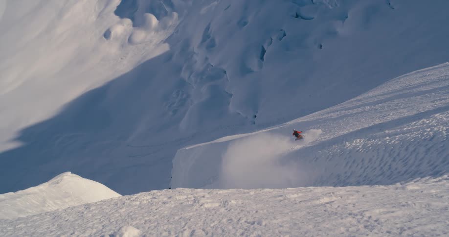 A snowboarder descends a steep mountain slope on a sunny day