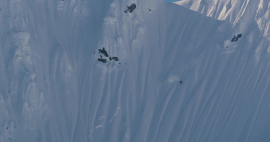 A skier descends a long steep mountain slope on a sunny day