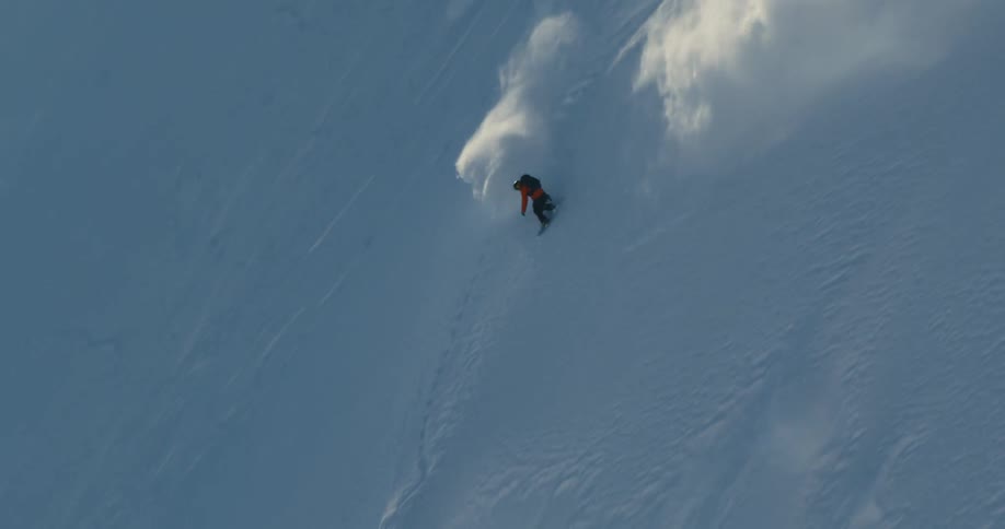 Man in a snowboard slides down the snow covered steep slope of a mountain