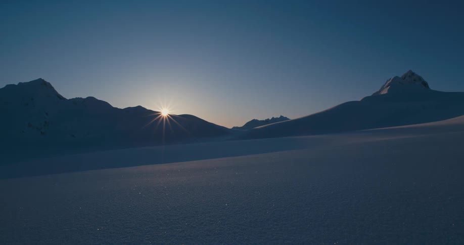 Sun sets behind snow covered mountain peaks