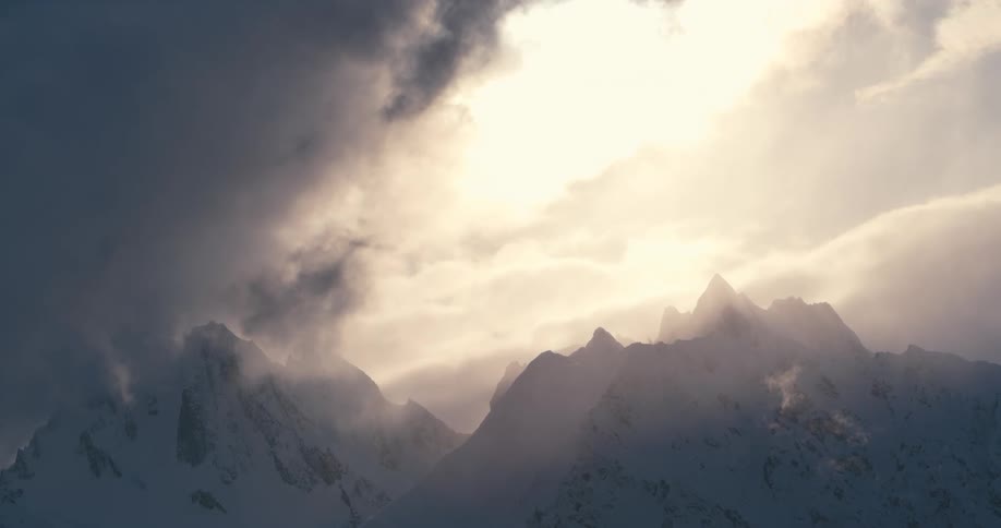 Jagged snow covered mountain ridge with heavy clouds and glowing sunlight