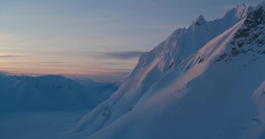 Red sky hovers over horizon behind snow covered mountains and valley