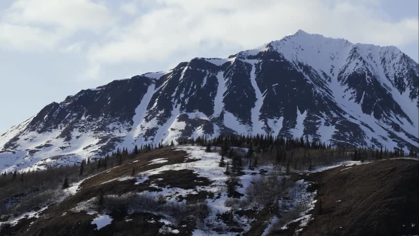 Aerial wrap around a vast mountain range with trees below
