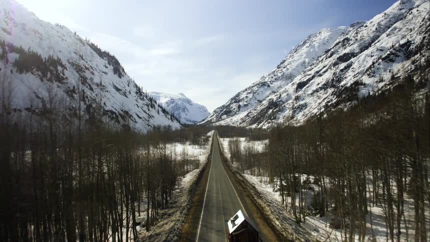 A truck tows a small cabin down a road through a deep snowy valley