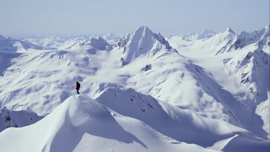 Aerial wrap around a man on the summit of a massive mountain range