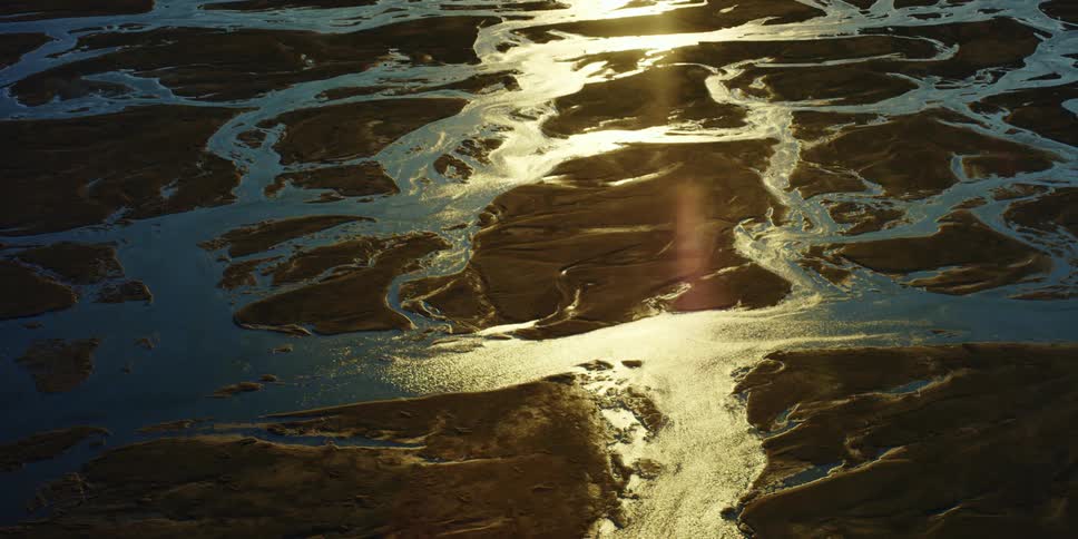 Sun shines across land full of streams rivers and rivulets leaving part of them in shadow
