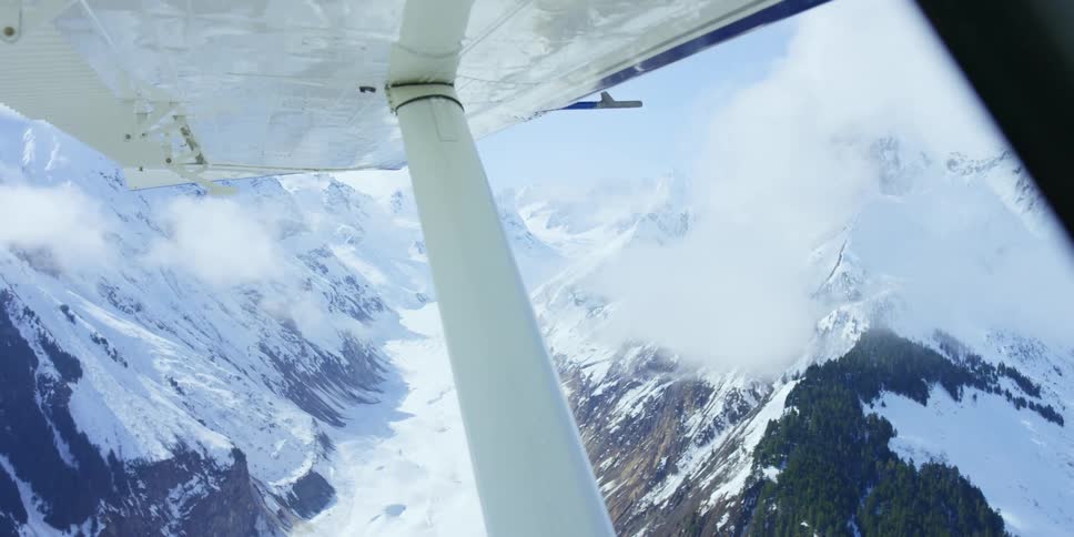 View of snow covered mountains from under plane wing