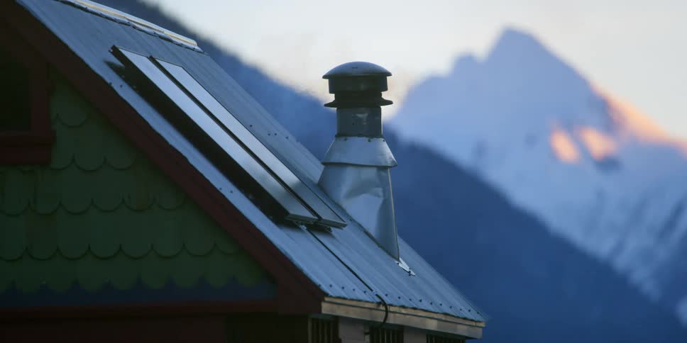 Smoke rises from the chimney of a small house near mountains