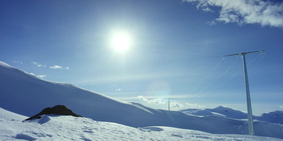 Ice covered power lines run across a snowy mountain range on a clear winter day