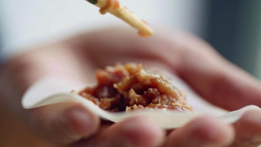 A woman uses chopsticks to add a meat filling to a dumpling wrapper