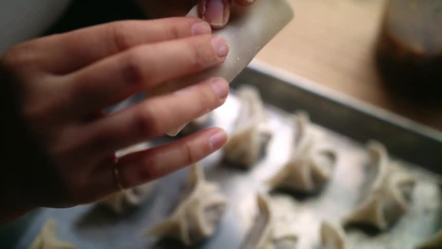 A woman carefully places prepares a small dumpling and pinches it closed