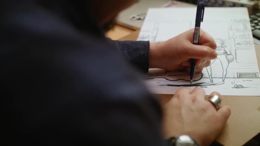 A man uses a black marker to shade a drawing