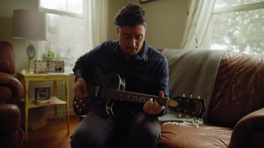 Man sitting on living room sofa playing electric guitar