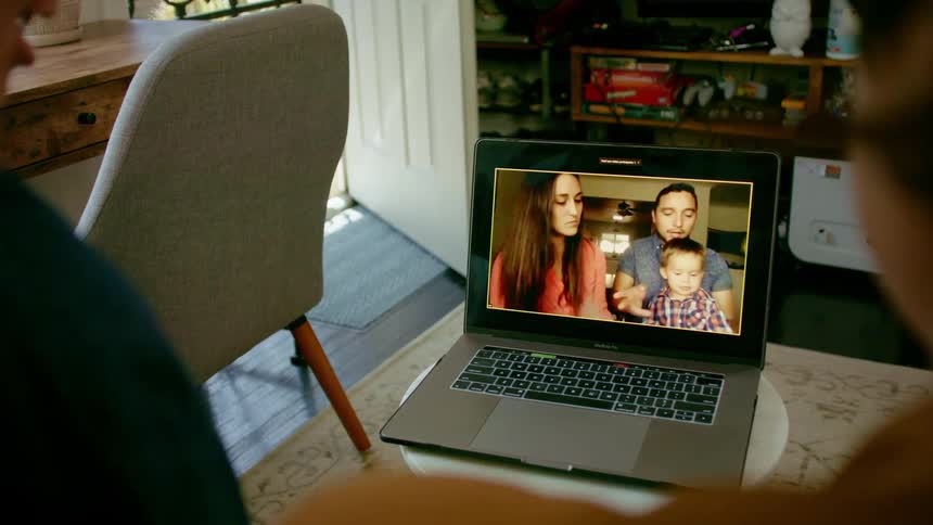 Two people sit in front of a laptop having a video call with a man woman and child