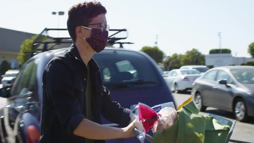 Man wearing face mask pushes grocery cart through parking lot