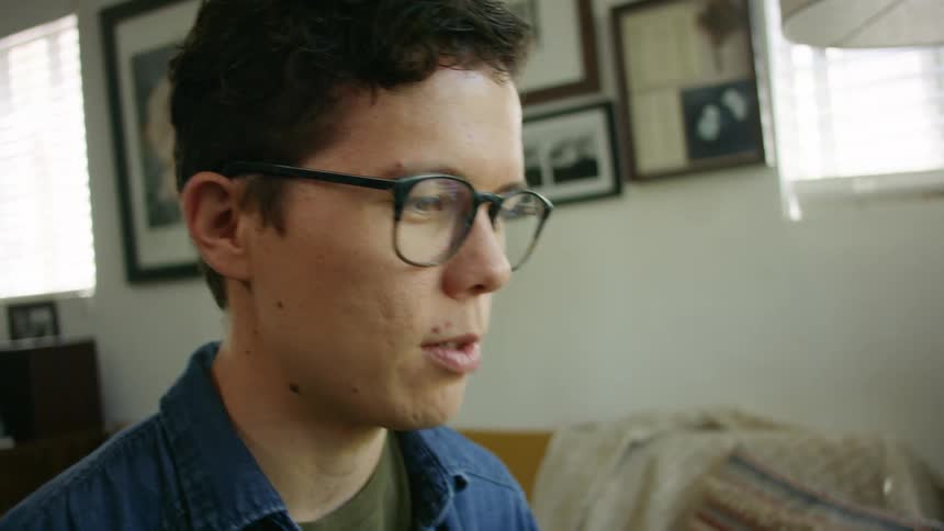 Man adjusts glasses while talking animatedly in living room